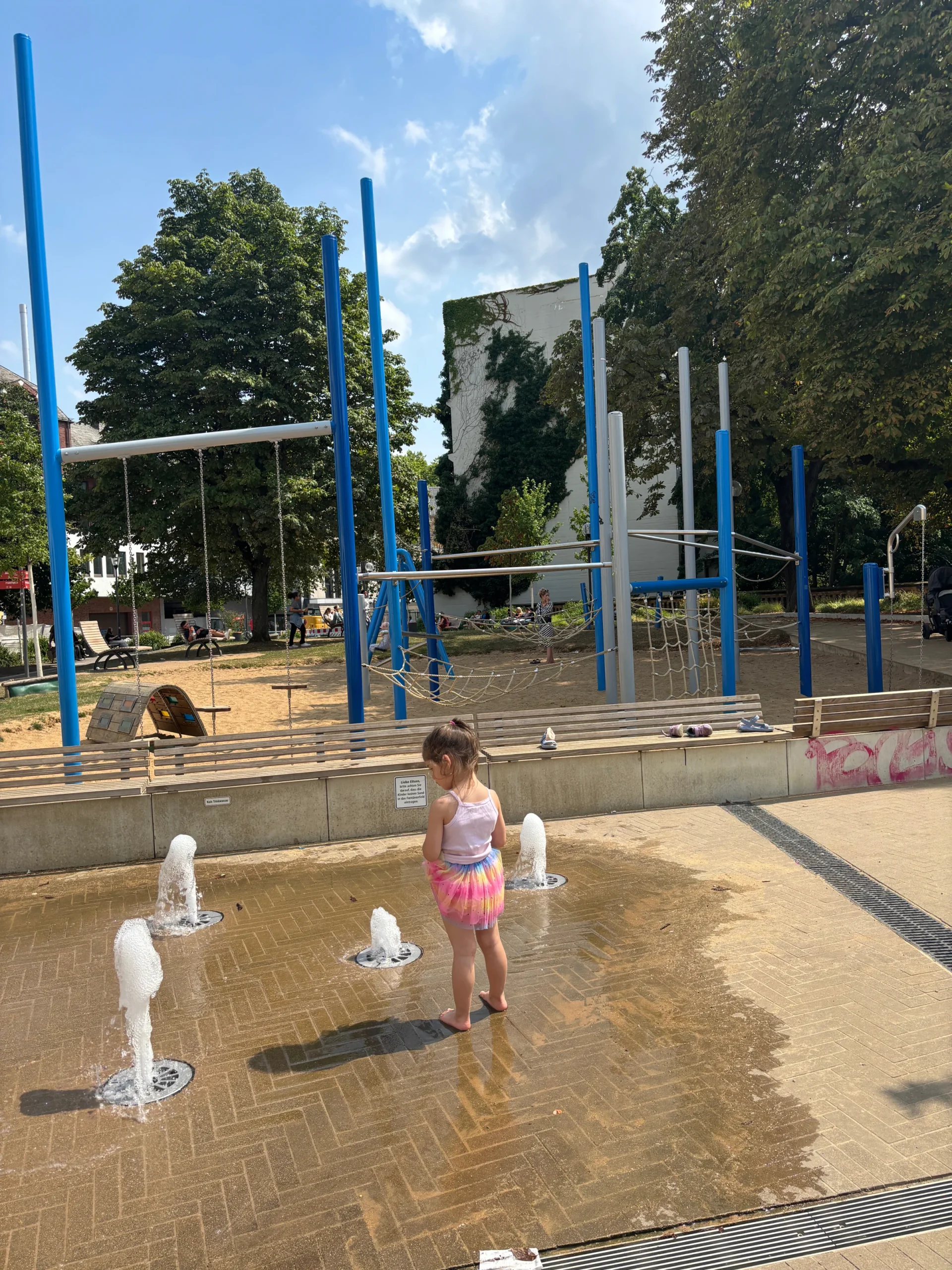 Kind spielt barfuß an Wasserfontänen auf einem Spielplatz.
