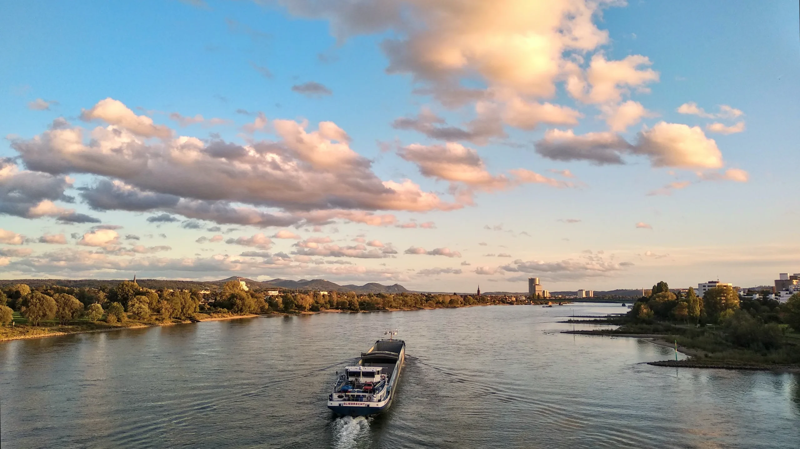 Frachtschiff auf dem Rhein vor der Bonner Skyline bei Abendlicht.
