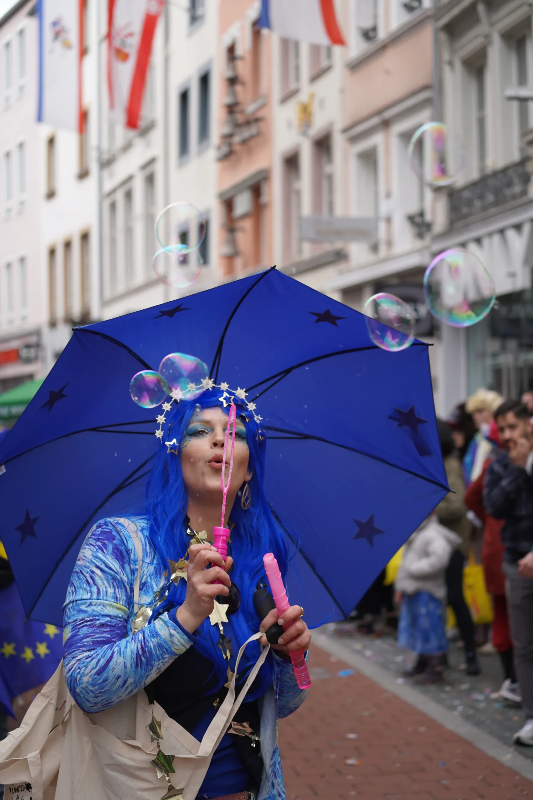 Person in blauem Europa-Kostüm bläst Seifenblasen beim Straßenkarneval.