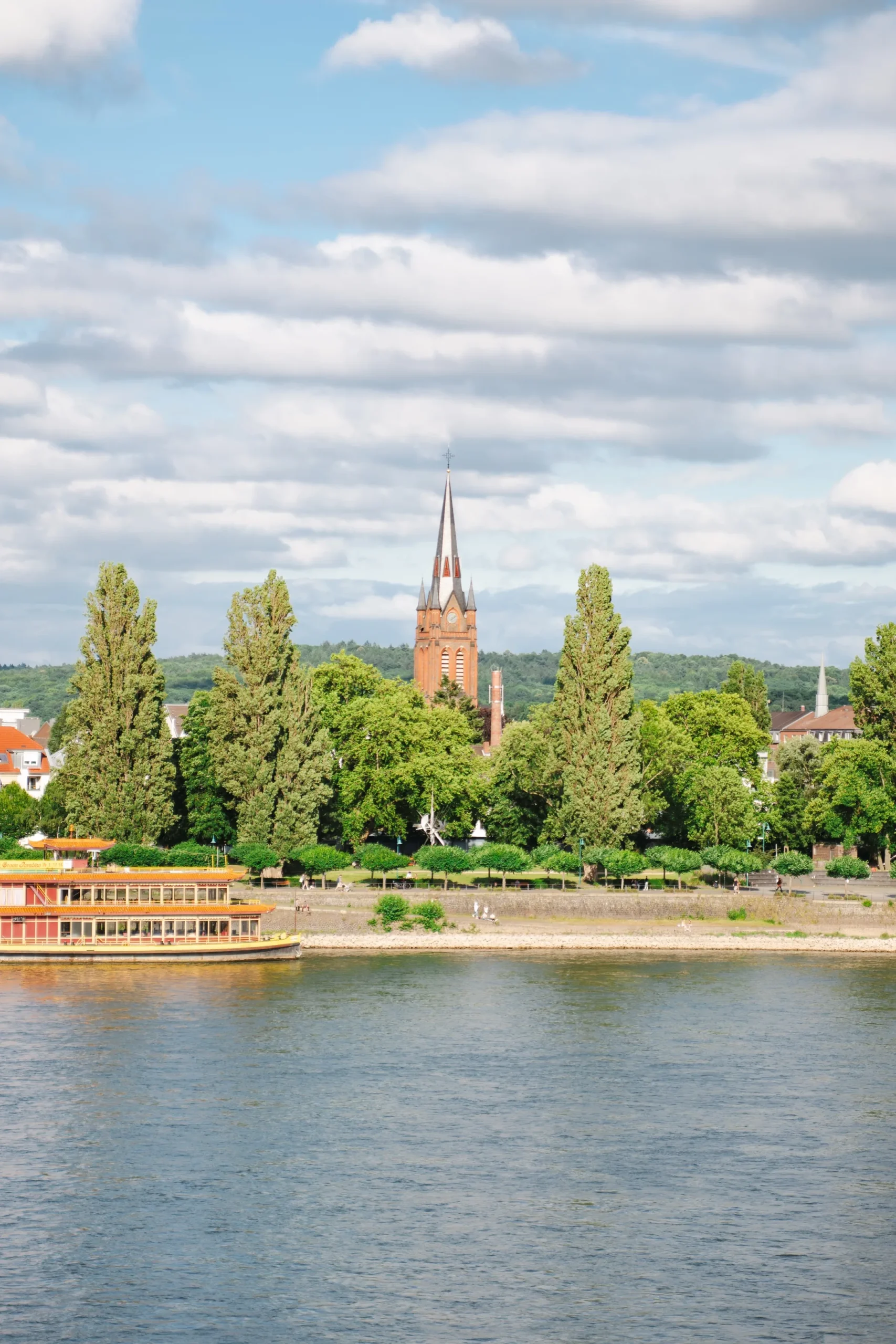 Blick über den Rhein auf die Kirche St. Josef in Beuel; im Vordergrund fährt ein Schiff.