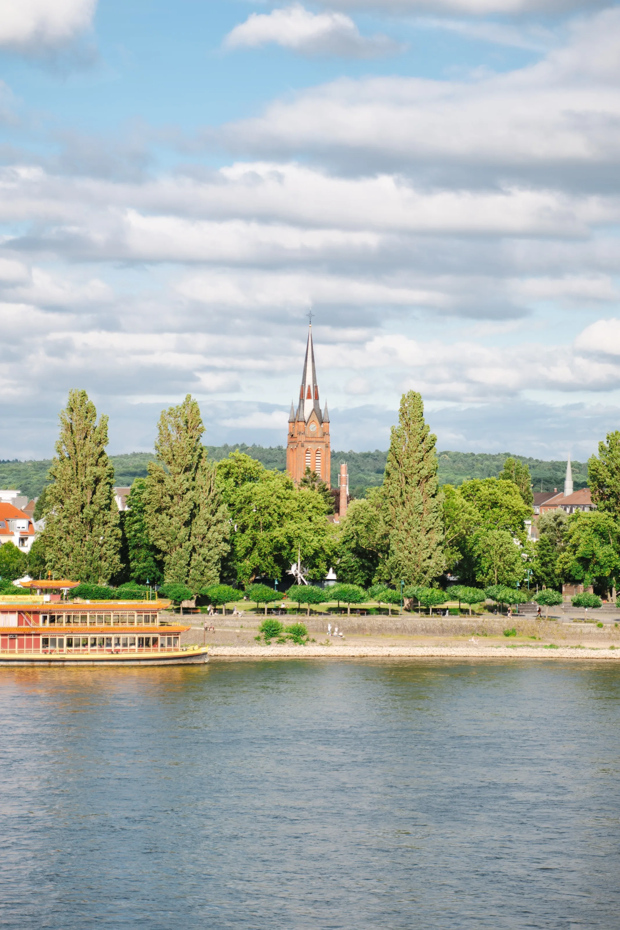 Blick über den Rhein auf die Kirche St. Josef in Beuel; im Vordergrund fährt ein Schiff.