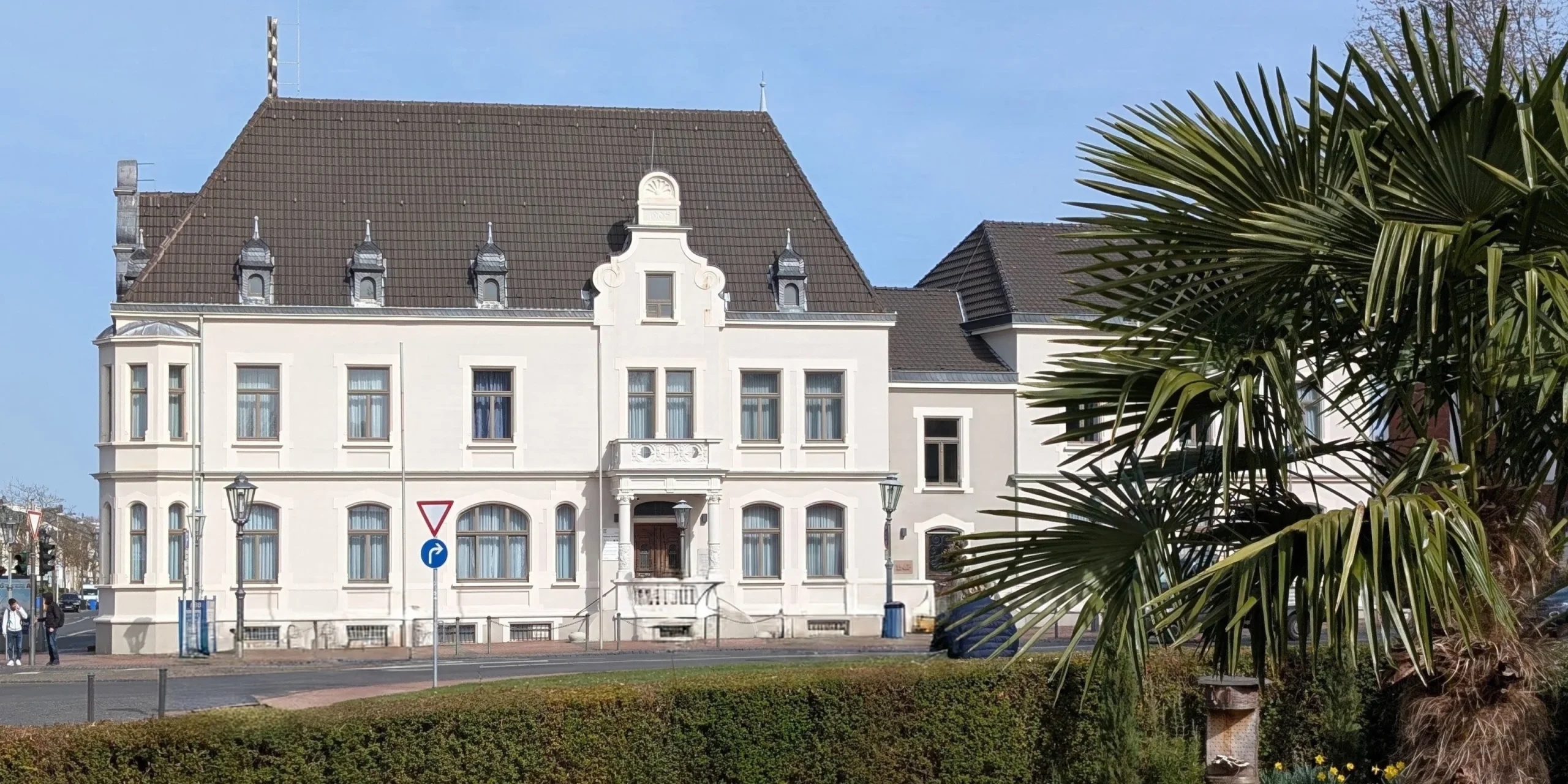 Helles historisches Gebäude mit Palmen im Vordergrund.