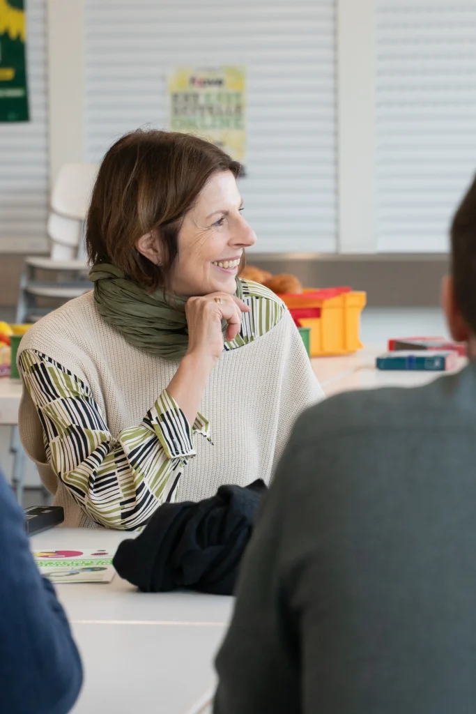 Eine Frau sitzt an einem Tisch und spricht mit Menschen im Vordergrund.